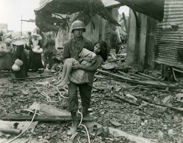 American Soldier Helping Injured Filipina Girl Through War Rubble, 1945